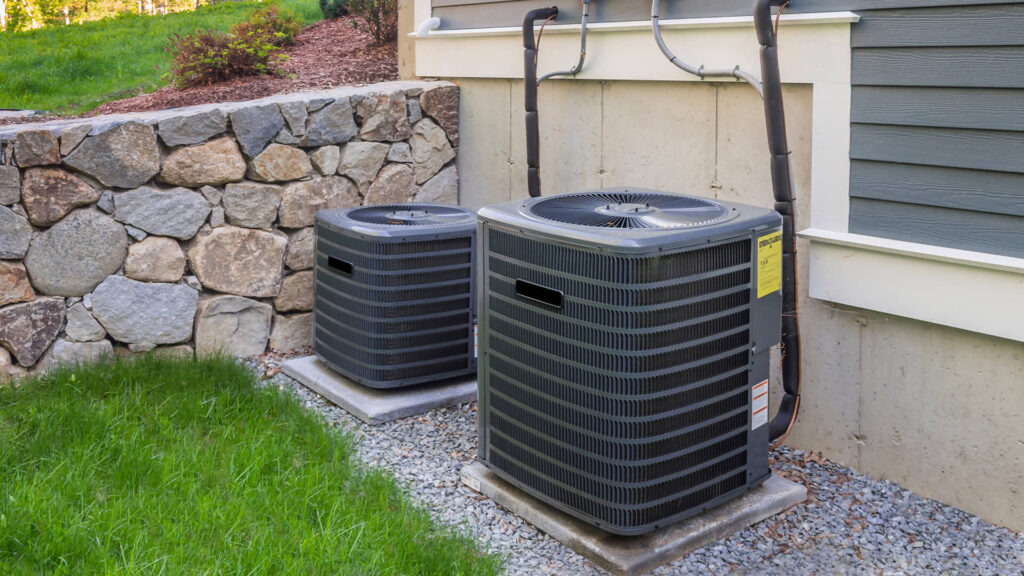 Two central air conditioning units installed beside a home
